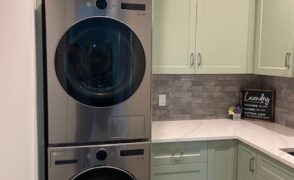 Algonquin Highlands laundry room cabinets in sage green shaker style, built around a stacked washer and dryer, with crown moulding, a bank of drawers and a white countertop, by Palmer's Woodworking.