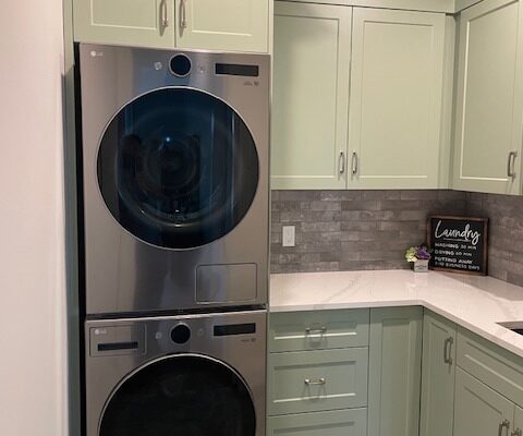 Algonquin Highlands laundry room cabinets in sage green shaker style, built around a stacked washer and dryer, with crown moulding, a bank of drawers and a white countertop, by Palmer's Woodworking.