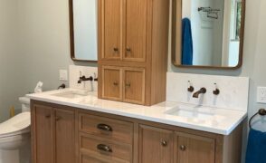 Custom light wood double bathroom vanity with a centre tower cabinet, crown moulding, four drawers with bronze cup pulls and a white countertop with two sinks, designed, built and installed by Palmer's Woodworking in Algonquin Highlands, Ontario.
