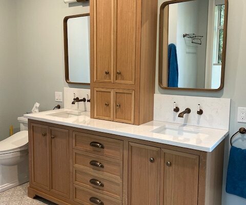Custom light wood double bathroom vanity with a centre tower cabinet, crown moulding, four drawers with bronze cup pulls and a white countertop with two sinks, designed, built and installed by Palmer's Woodworking in Algonquin Highlands, Ontario.